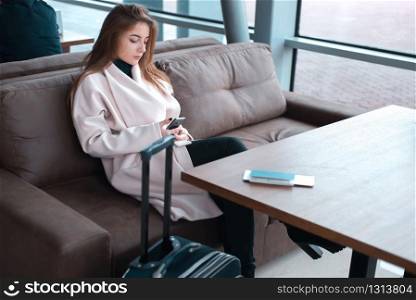 Young female passenger at the airport, using phone while waiting for her flight