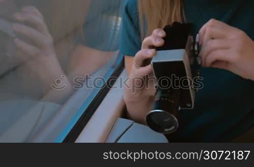 Young female passenger in the train using retro video camera to film outside view