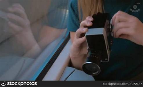 Young female passenger in the train using retro video camera to film outside view