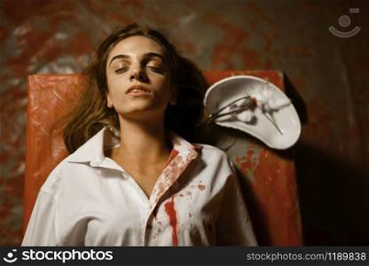 Young female patient lying on surgical table, top view, psychiatrist blood butcher, mental hospital basement. Victim of doctor maniac in clinic for the mentally ill
