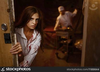 Young female patient trying to get away from crazy male psychiatrist maniac, mental hospital basement. Victim of bloody butcher doctor in clinic for the mentally ill