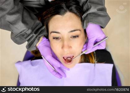 Young female patient visiting dentist office.Beautiful woman sitting at dental chair with open mouth during oral checkup while doctor working at teeth. High quality photo. Young female patient visiting dentist office.Beautiful woman sitting at dental chair with open mouth during oral checkup while doctor working at teeth
