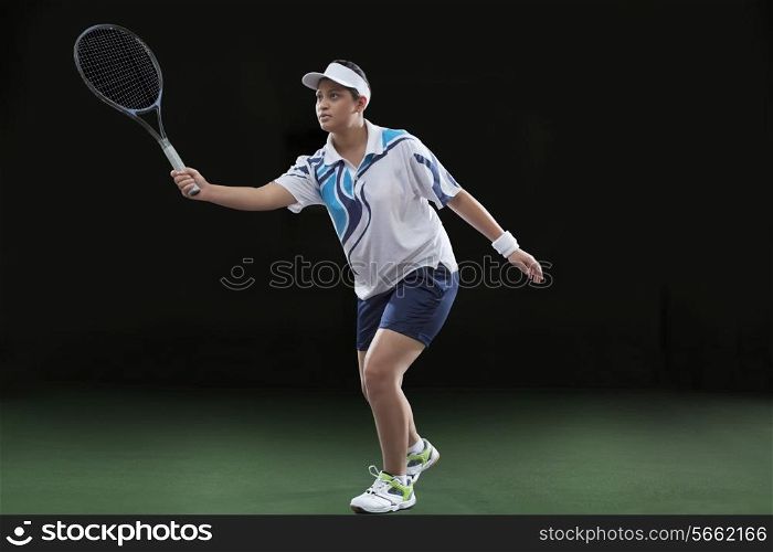 Young female player in sportswear playing tennis over black background