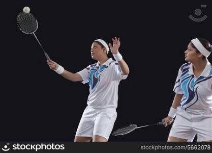 Young female player looking at partner hitting shuttlecock with racket over black background