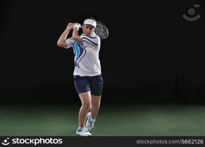 Young female player playing tennis over black background