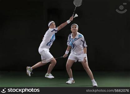 Young female players in sportswear playing doubles badminton against black background