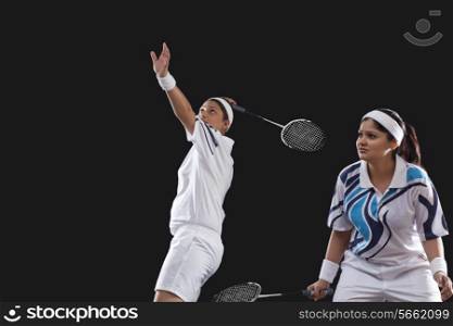 Young female players playing doubles badminton isolated over black background