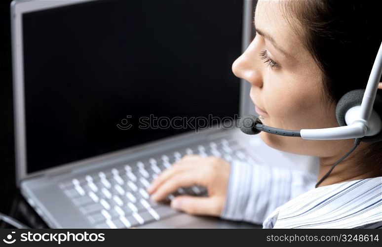 Young female recepcionist works on laptop and recieves phone calls on headset.