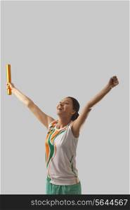 Young female relay runner celebrating victory against gray background
