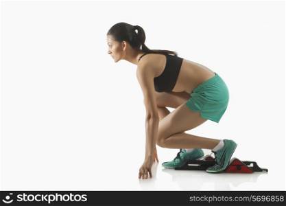 Young female runner at starting block against white background