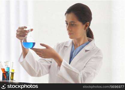 Young female scientist looking at liquid in beaker