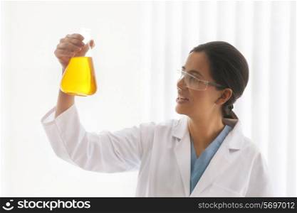 Young female scientist looking at yellow liquid in beaker