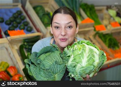 young female seller wearing apron holding fresh cabbage on market