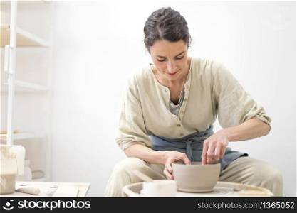 Young female sitting by table and making clay or ceramic mug in her working studio