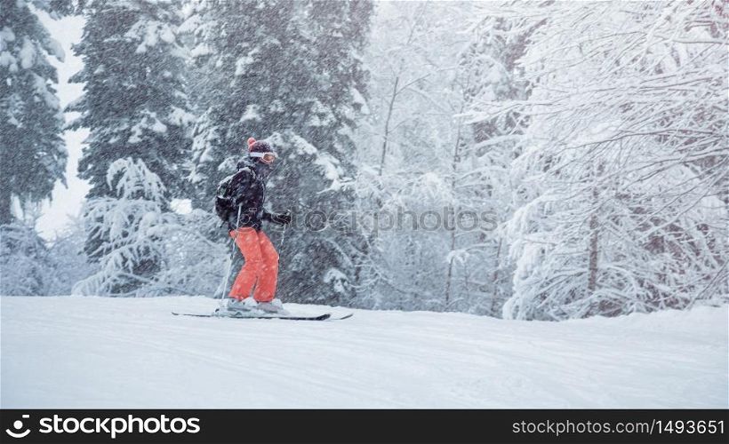 Young female skier sliding down the slope under snowfall