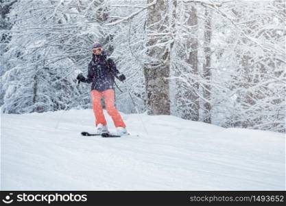 Young female skier sliding down the slope under snowfall