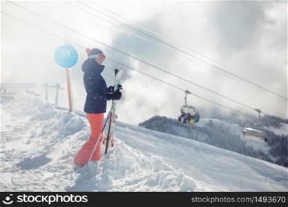 Young female skier standing on ski slope, mountains and chairlift on background. Sochi; Krasnaya Polyana, Russia