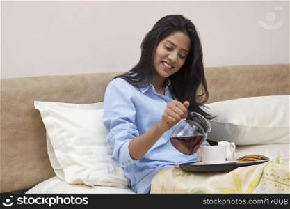 Young female smiling while having morning tea and breakfast in bed