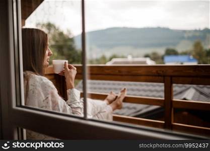 Young female standing after taking a shower in the morning on balcony of the hotel. holding a cup of coffee or tea in her hands. Looking outside nature forest and Mountain.. Young female standing after taking a shower in the morning on balcony of the hotel. holding a cup of coffee or tea in her hands. Looking outside nature forest and Mountain