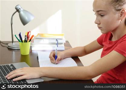 Young female student doing homework on a laptop in her room.