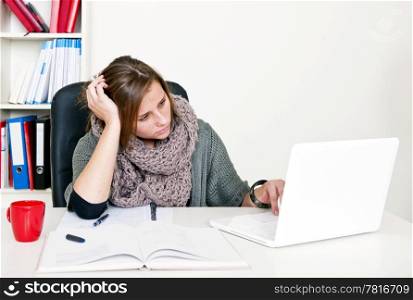 Young female student doing internet research whilst studying her textbooks behind her desk