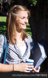 Young female student, holding a dossier with notes and a cup of coffee, smiling in the sunlight