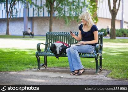 Young female student using cell phone while sitting in college campus