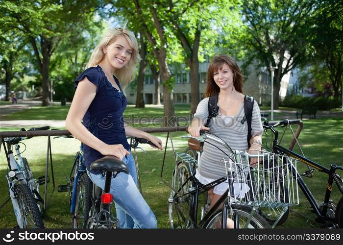 Young female students standing with bicycle at college campus lawn