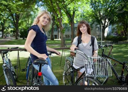 Young female students standing with bicycle at college campus lawn
