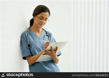 Young female surgeon writing notes while leaning on wall