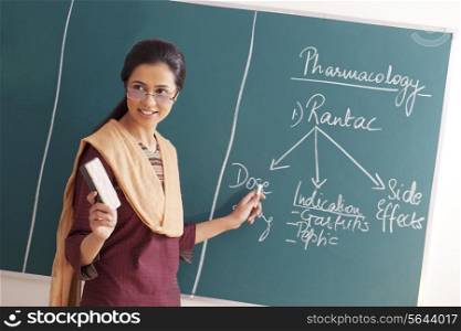 Young female teacher explaining a lesson while holding chalk and duster against green board