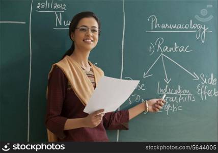 Young female teacher explaining a lesson while standing against chalkboard