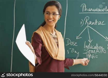 Young female teacher explaining a lesson while standing against chalkboard