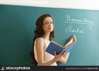Young female teacher explaining a lesson while standing against green board