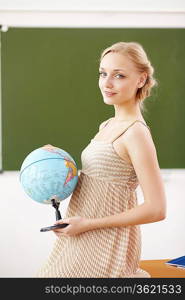 Young female teacher holding a globe at school