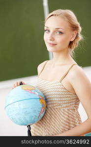 Young female teacher holding a globe at school