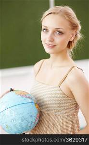 Young female teacher holding a globe at school