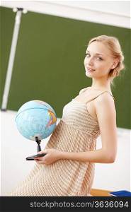 Young female teacher holding a globe at school