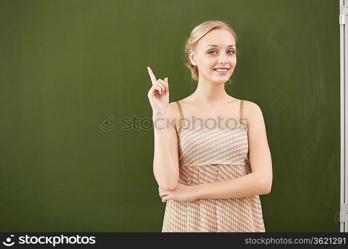 Young female teacher standing near blackboard at school