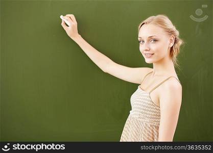 Young female teacher standing near blackboard at school