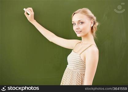 Young female teacher standing near blackboard at school