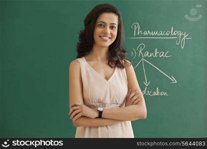Young female teacher standing with arms crossed against green board