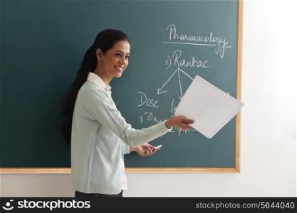 Young female teacher with papers explaining by chalkboard