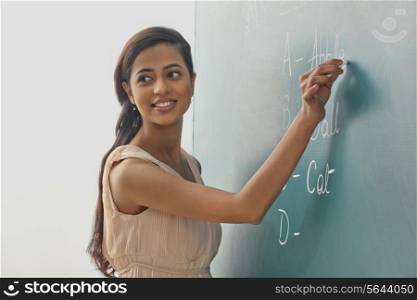 Young female teacher writing on green board while looking away