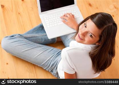 Young female teenager with laptop sitting on wooden floor
