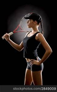 Young female tennis player posing with racket on black background