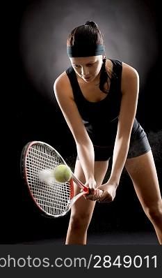 Young female tennis player ready to hit ball black background
