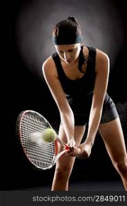 Young female tennis player ready to hit ball black background