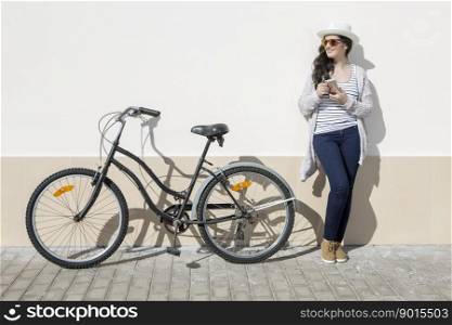 Young female tourist with smartphone standing nearby bike against wall in Lanzarote, Spain. . Young woman with gadget and bike