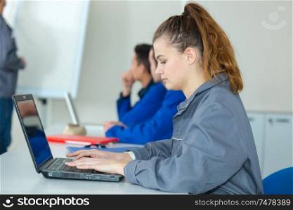 young female trainee in overalls using laptop in class